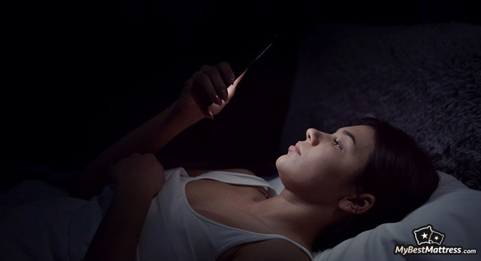 how to sleep less: woman scrolling her phone at night how to sleep less: woman scrolling her phone at night